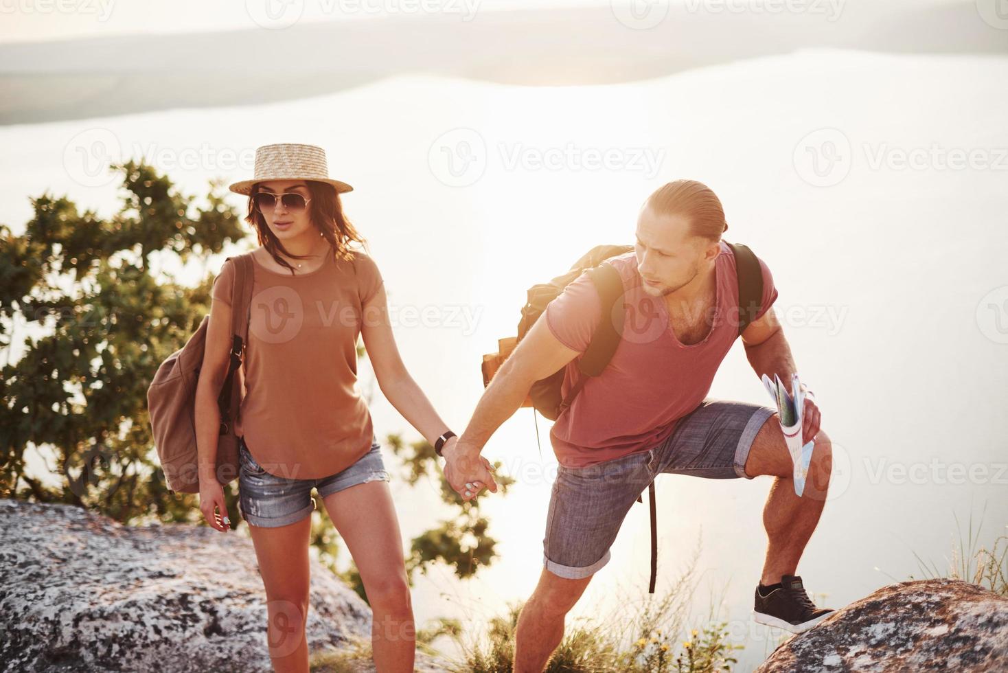 sintiendo confianza. pareja joven ha decidido pasar sus vacaciones de forma activa en el borde de la hermosa roca con el lago al fondo foto