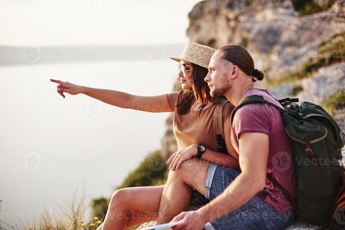 Young couple resting from walking at the edge of the mountain. Wonders how far other coast is it photo