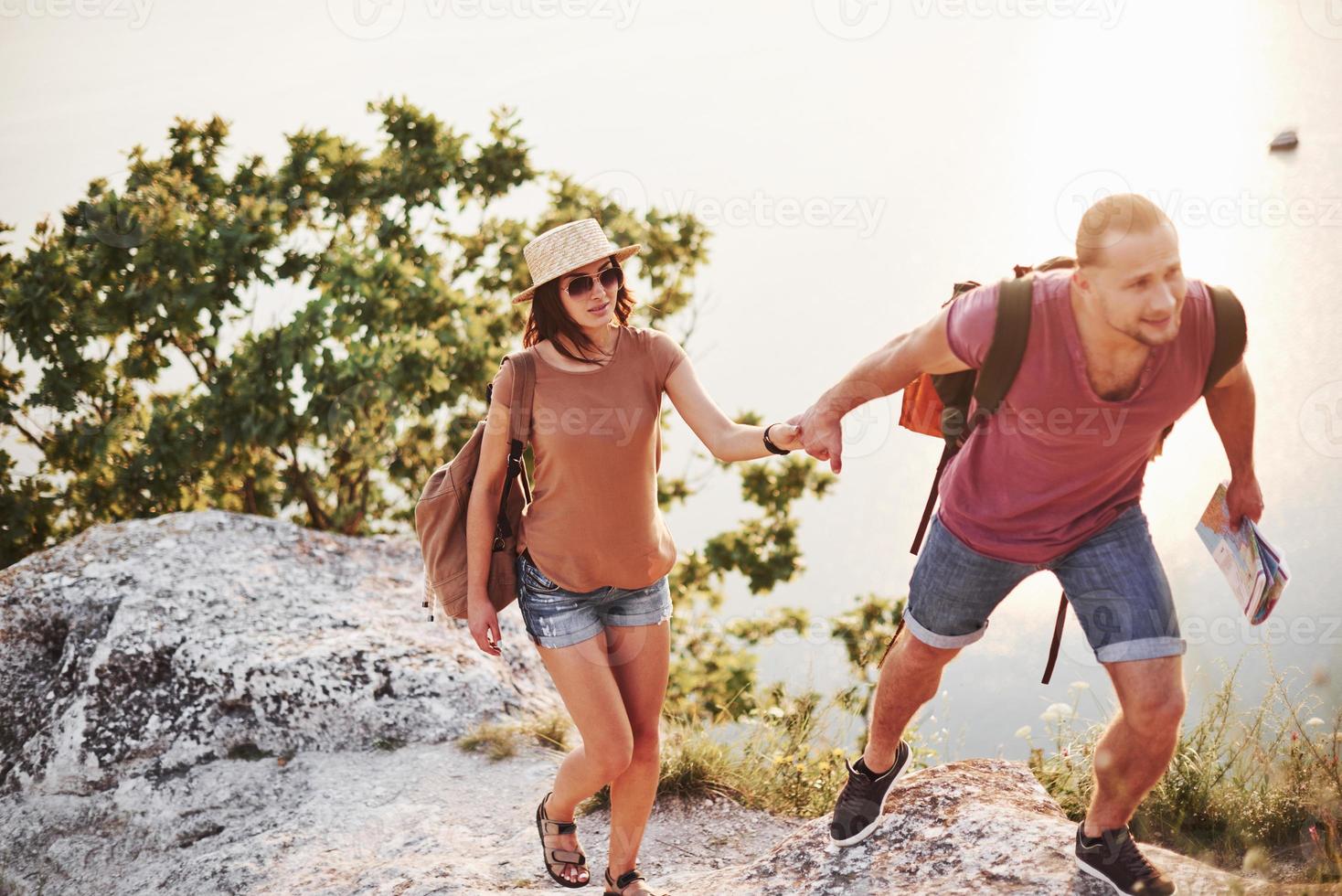 Parece que el hombre sabe a dónde ir. pareja joven ha decidido pasar sus vacaciones de forma activa en el borde de la hermosa roca con el lago al fondo foto