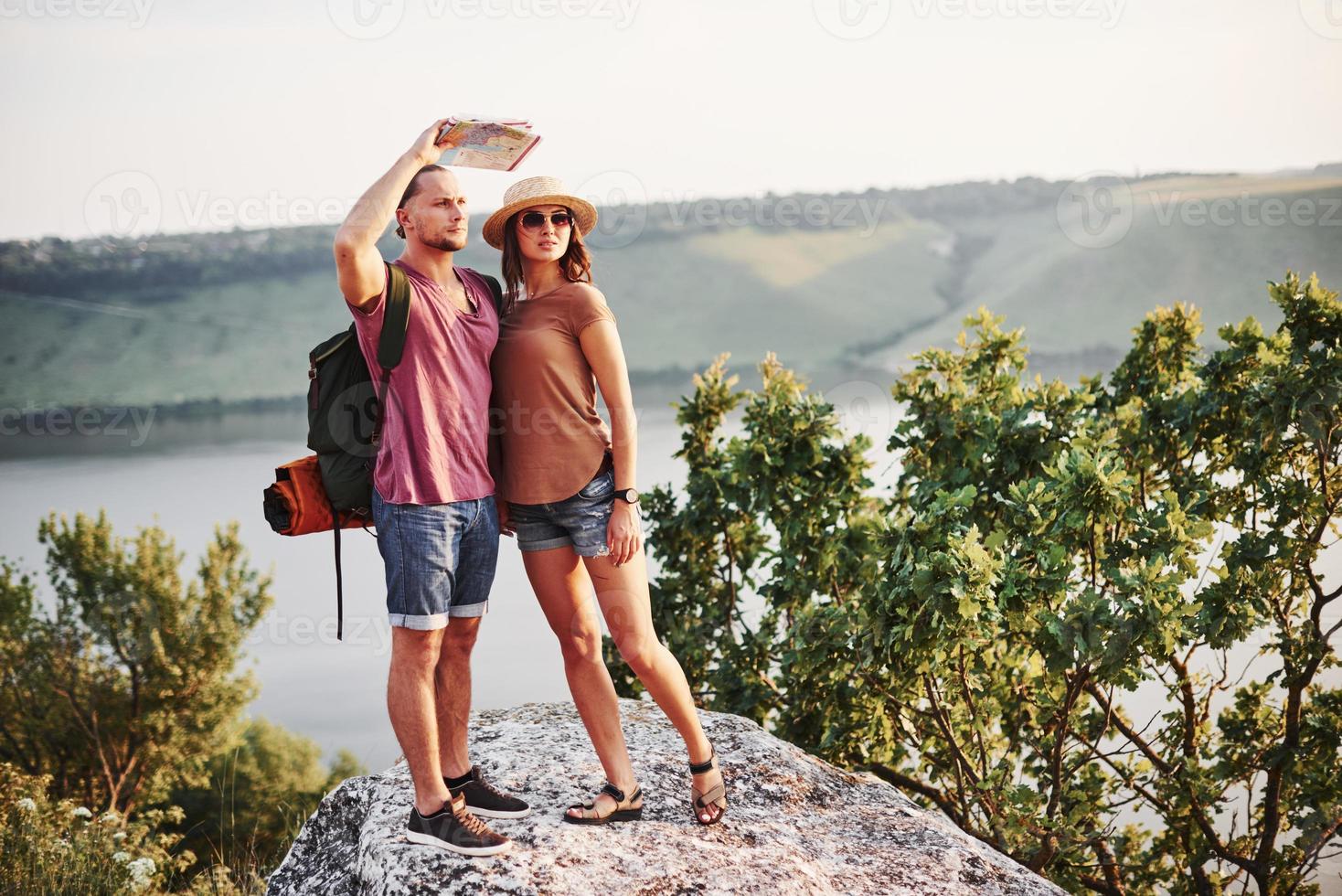 Maps don't lie, that man see adventures in front. Young couple have decided to spend their holiday in active way on the edge of the gorgeous rock with lake at background photo