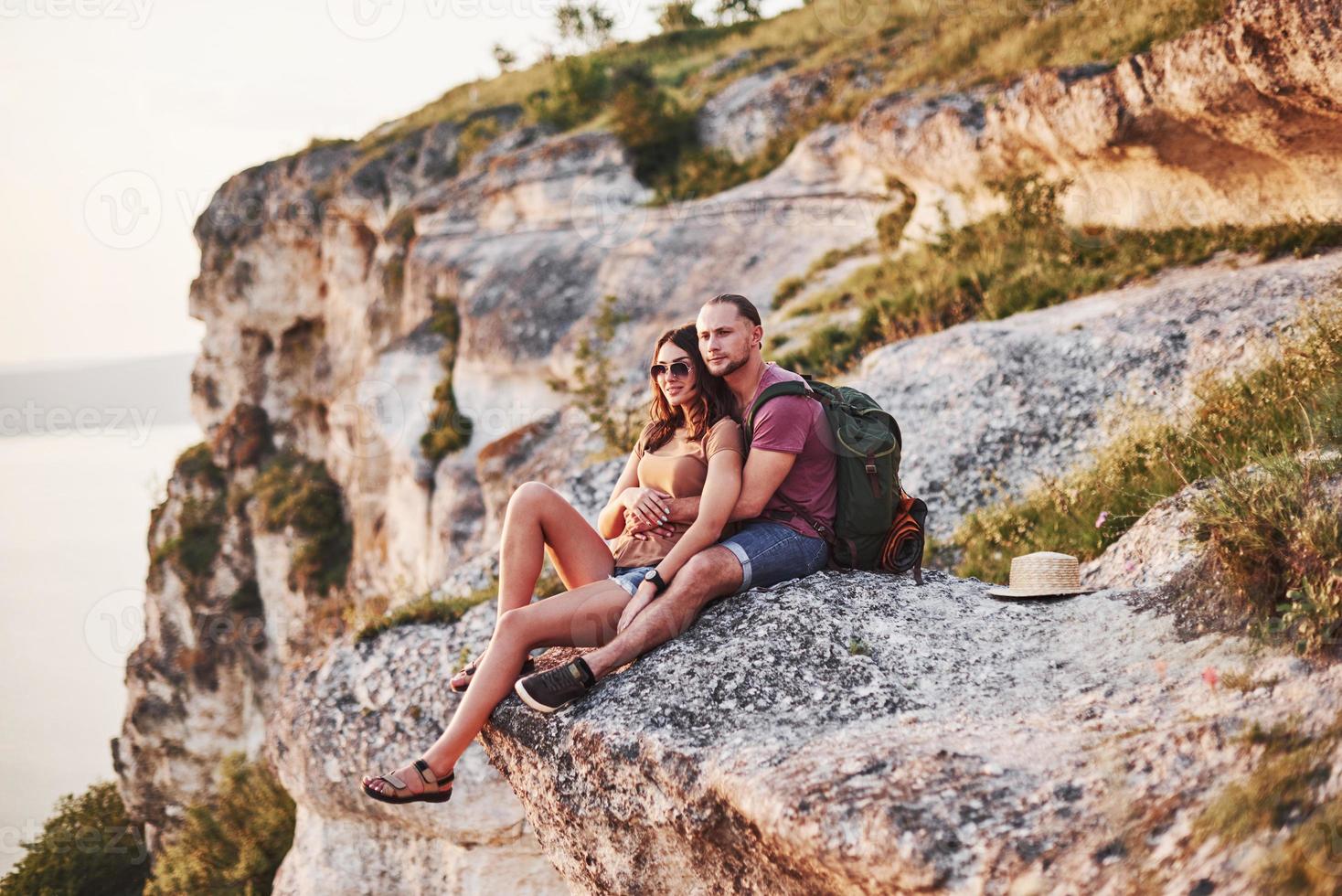 vista asombrosa. pareja joven descansando de caminar al borde de la montaña. se pregunta qué tan lejos está la otra costa foto