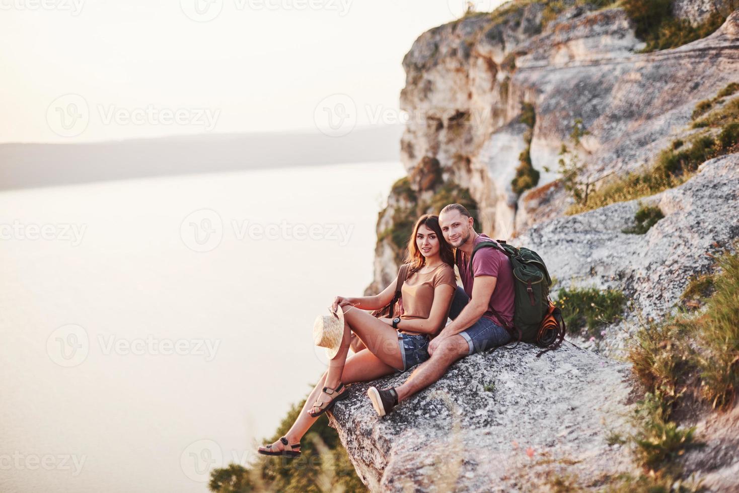 buen humor. pareja joven descansando de caminar al borde de la montaña. se pregunta qué tan lejos está la otra costa foto