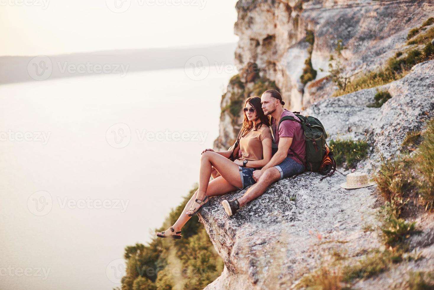 cerca del borde. pareja joven descansando de caminar al borde de la montaña. se pregunta qué tan lejos está la otra costa foto