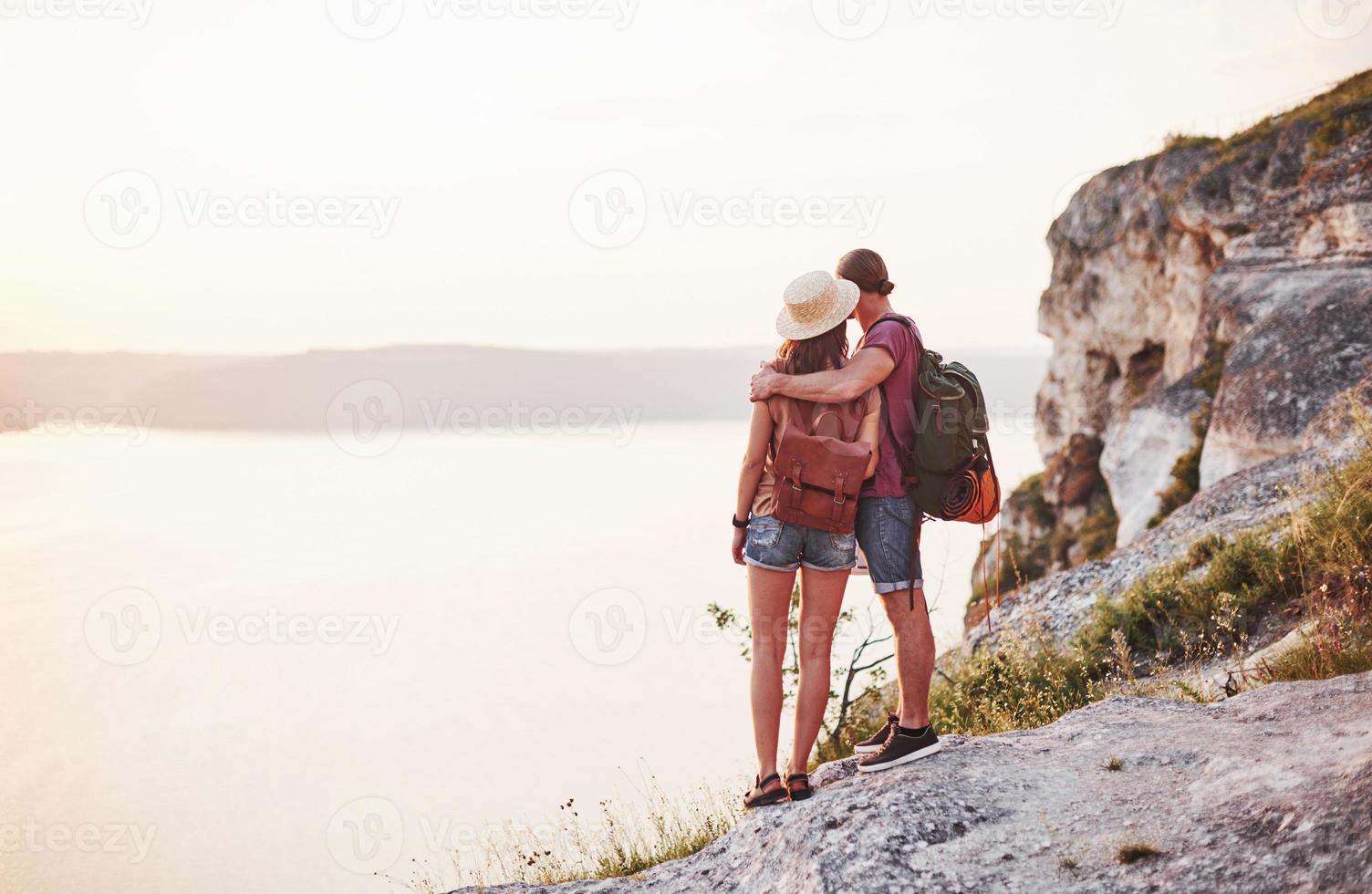 lejos. pareja joven ha decidido pasar sus vacaciones de forma activa en el borde de la hermosa roca con el lago al fondo foto