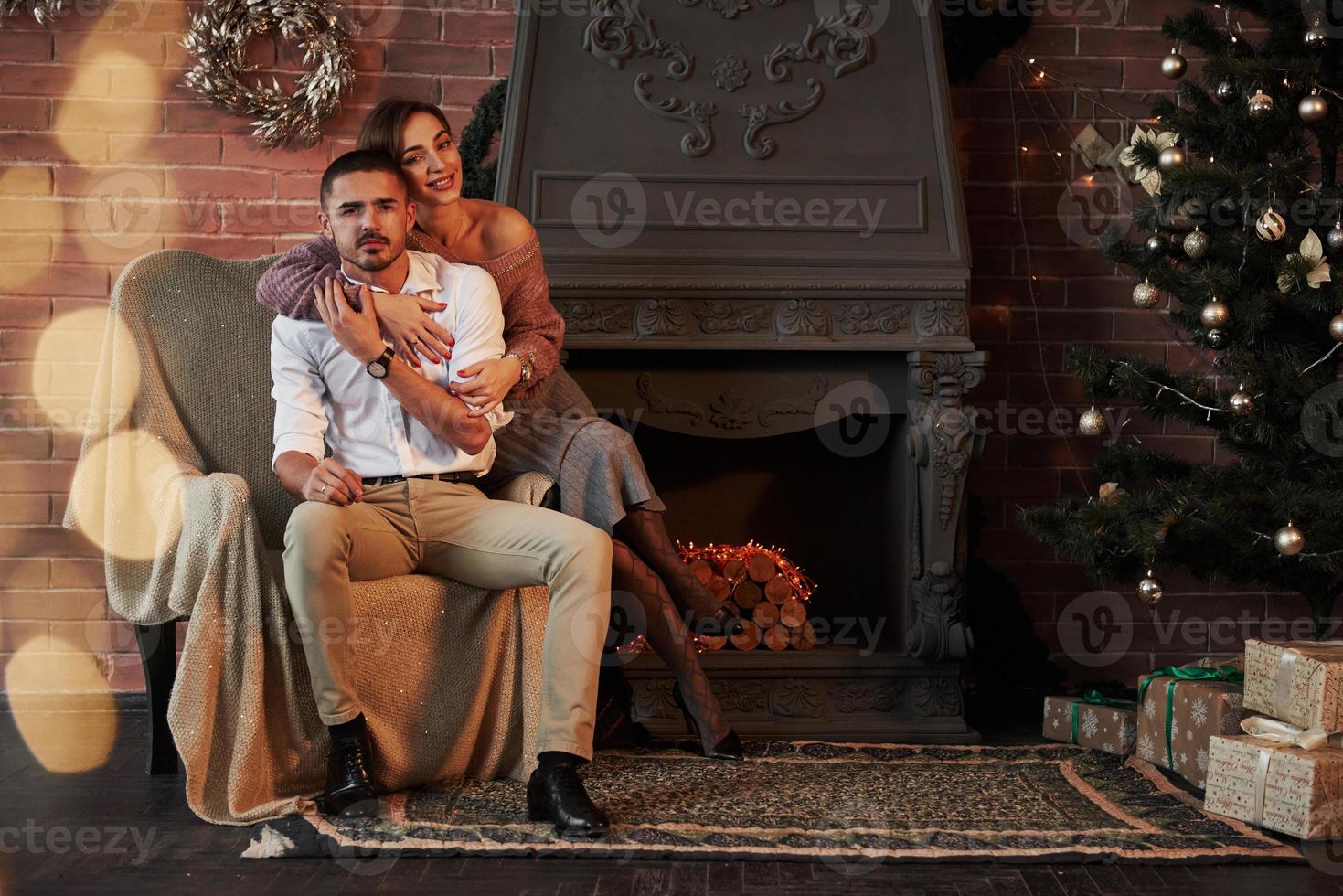 Luxury portrait. Beautiful young couple on the chair hugging in luxury room that is decorated holiday tree and garlands photo