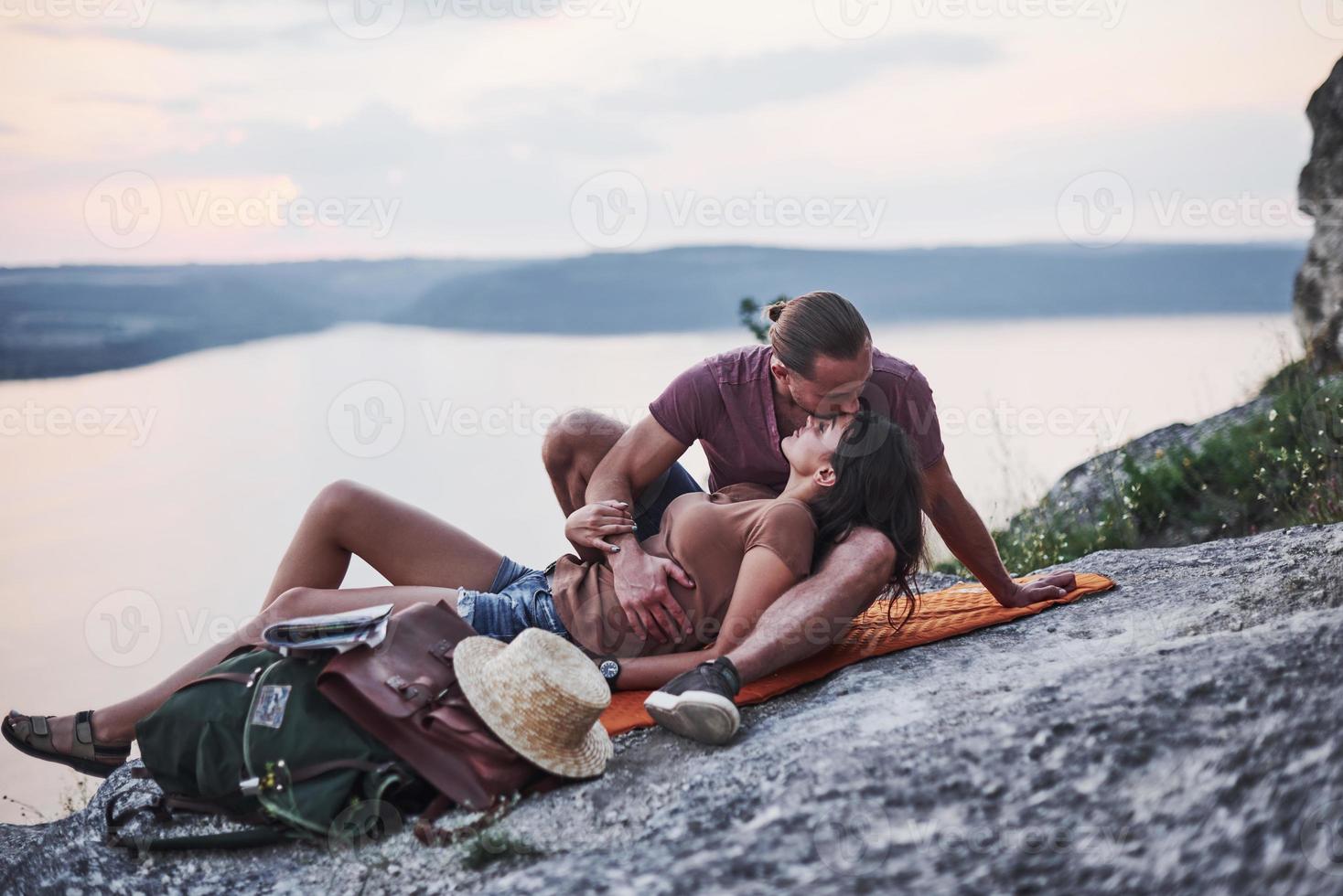 acostado para besar. pareja joven ha decidido pasar sus vacaciones de forma activa en el borde de la hermosa roca con el lago al fondo foto