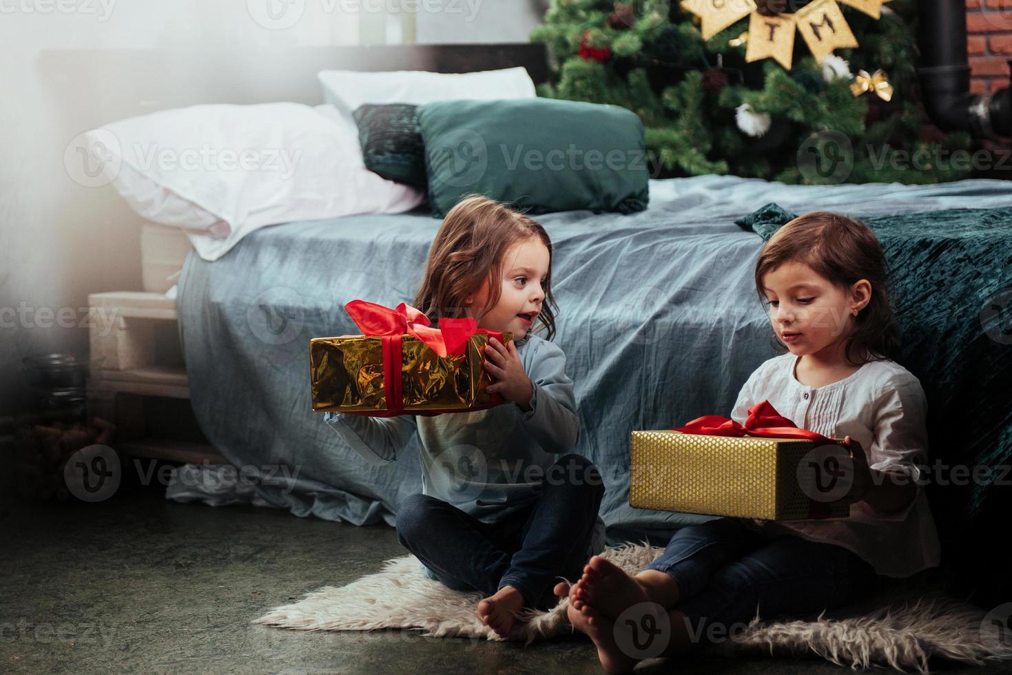 Precioso dormitorio decorado. vacaciones navideñas con regalos para estos dos niños que se sientan en el interior de la bonita habitación cerca de la cama foto