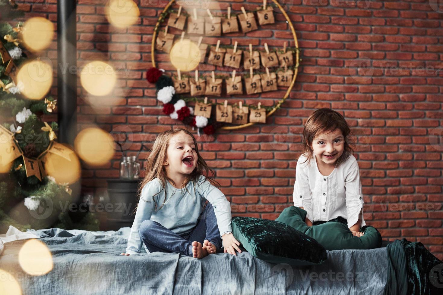 Loud laughing. Little girls having fun on the bed with holiday interior at the background photo