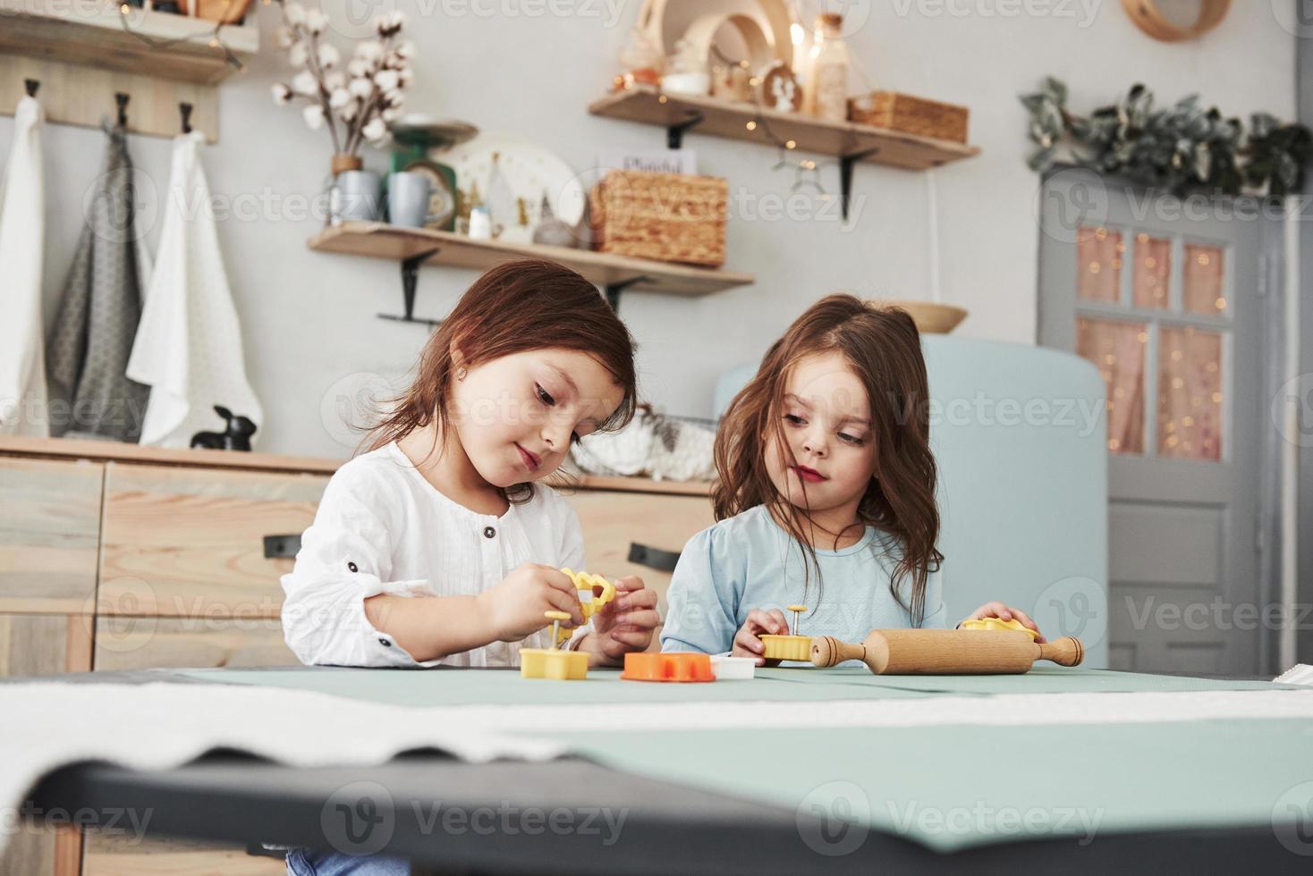 tiempo libre cuando los padres no están en casa. Dos niños jugando con juguetes amarillos y naranjas en la cocina blanca. foto