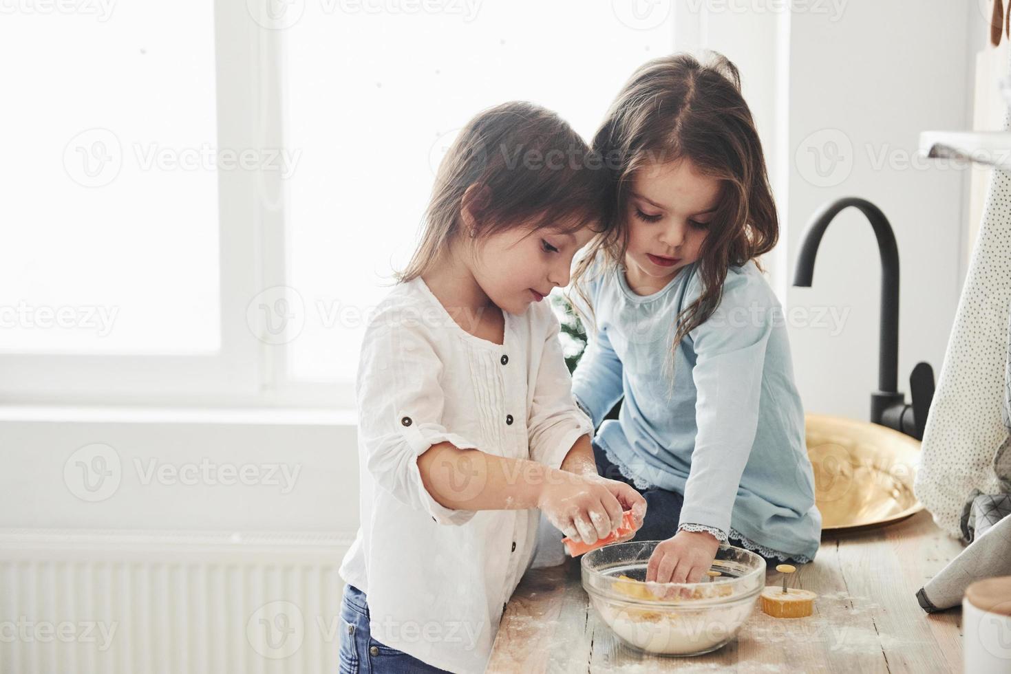 Amigos en edad preescolar aprendiendo a cocinar con harina en la cocina blanca foto