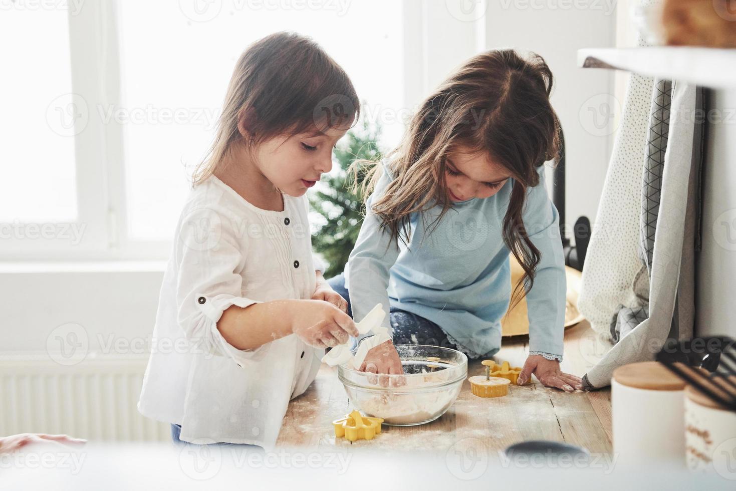 tales se centran en el trabajo. Amigos en edad preescolar aprendiendo a cocinar con harina en la cocina blanca foto