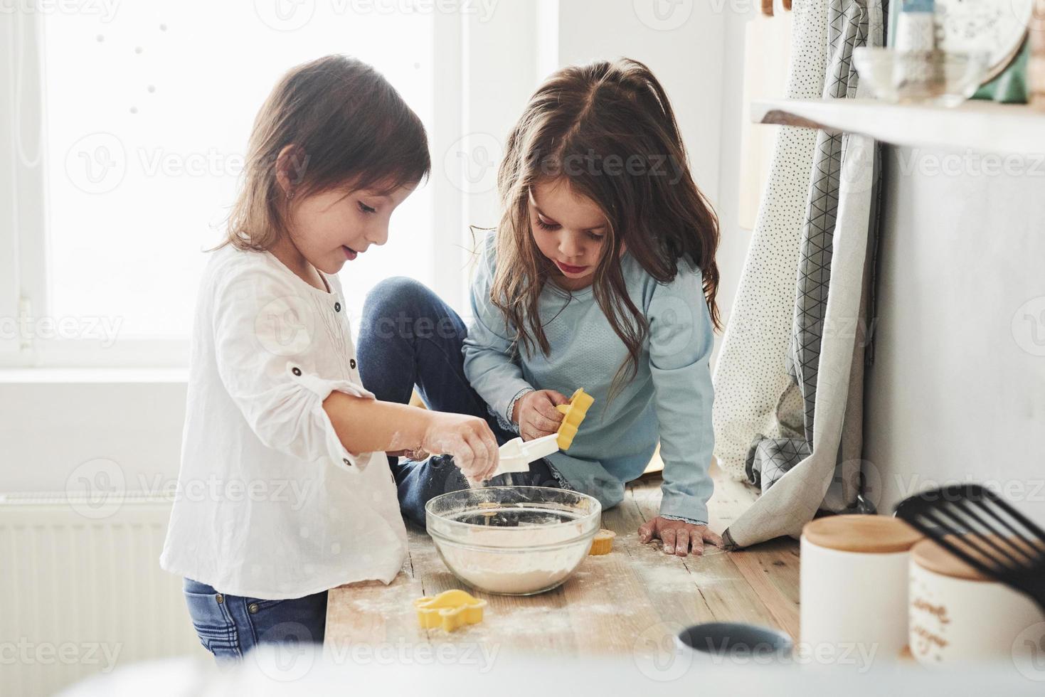 divertirse durante el proceso. Amigos en edad preescolar aprendiendo a cocinar con harina en la cocina blanca foto