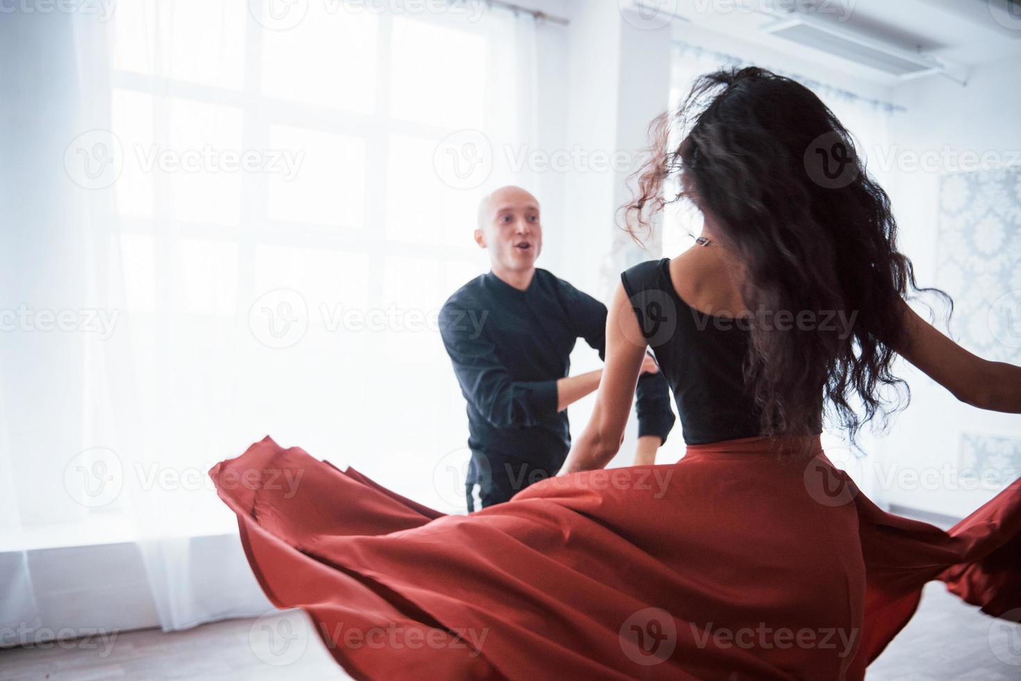 este es el arte. Joven bonita a mujer vestida de rojo y negro bailando con calvo en la sala blanca foto