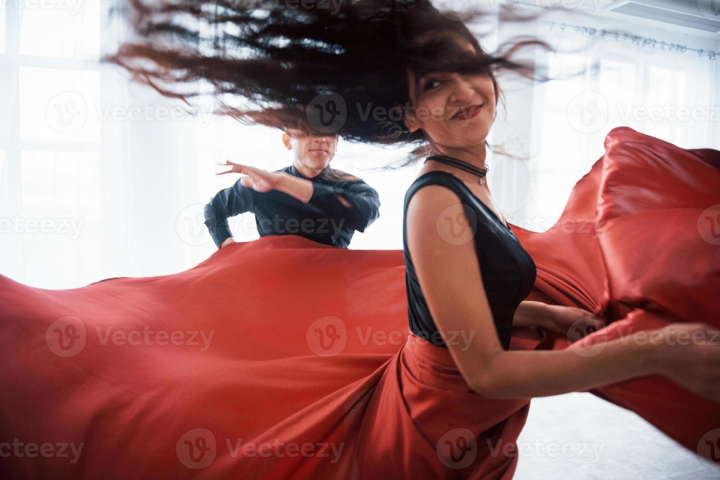 foto de movimiento. Joven bonita a mujer vestida de rojo y negro bailando con calvo en la sala blanca