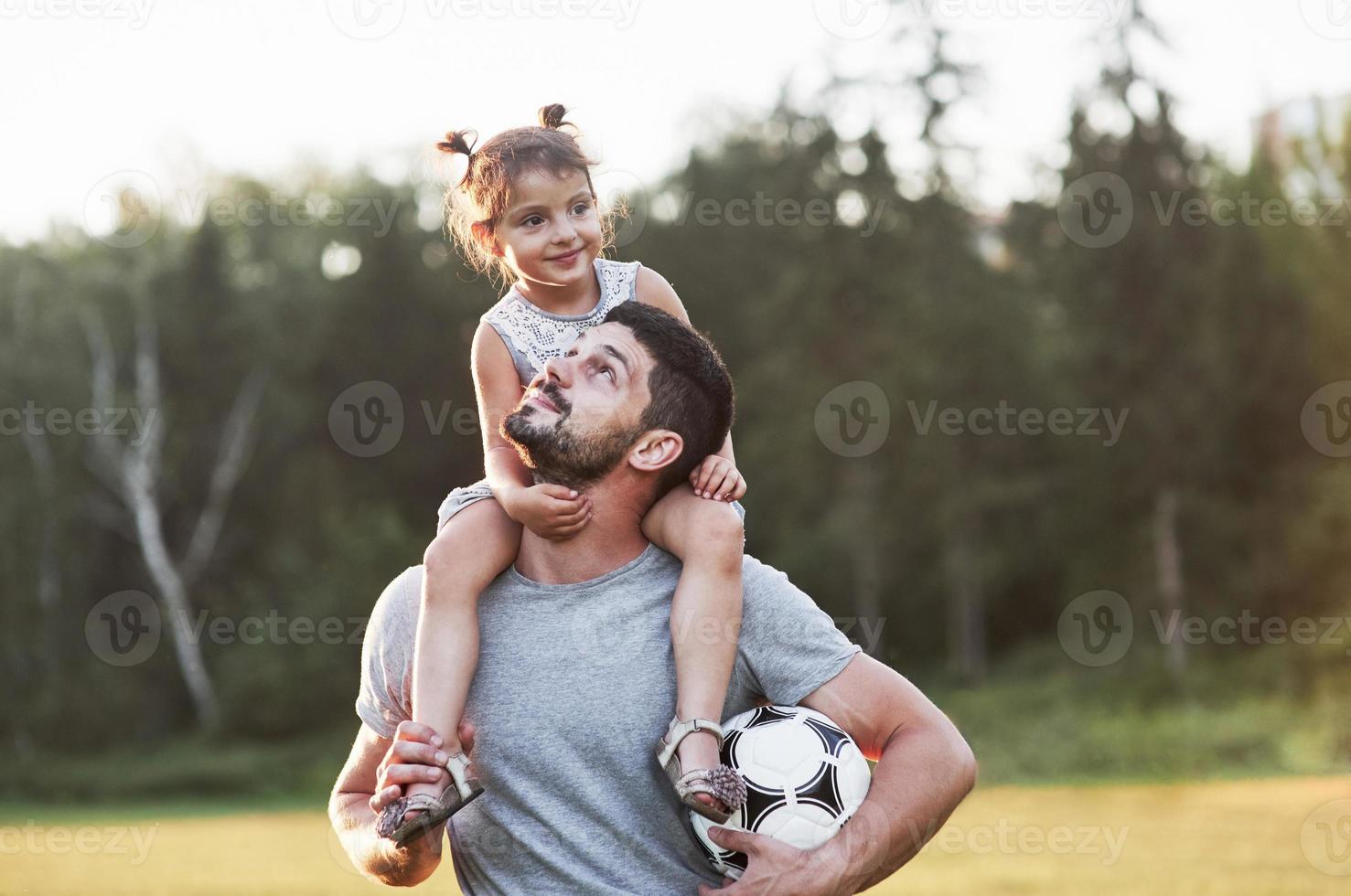 It's all about the family. Photo of dad with his daughter at beautiful grass and woods at background