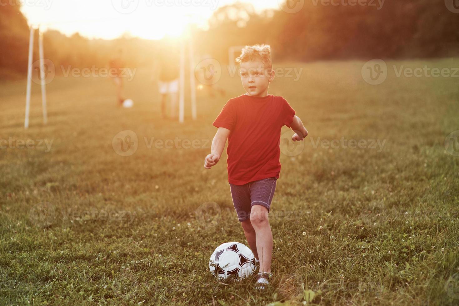 Where the rest of my team is go. Boy plays football at sunny warm day and going to score a goal photo