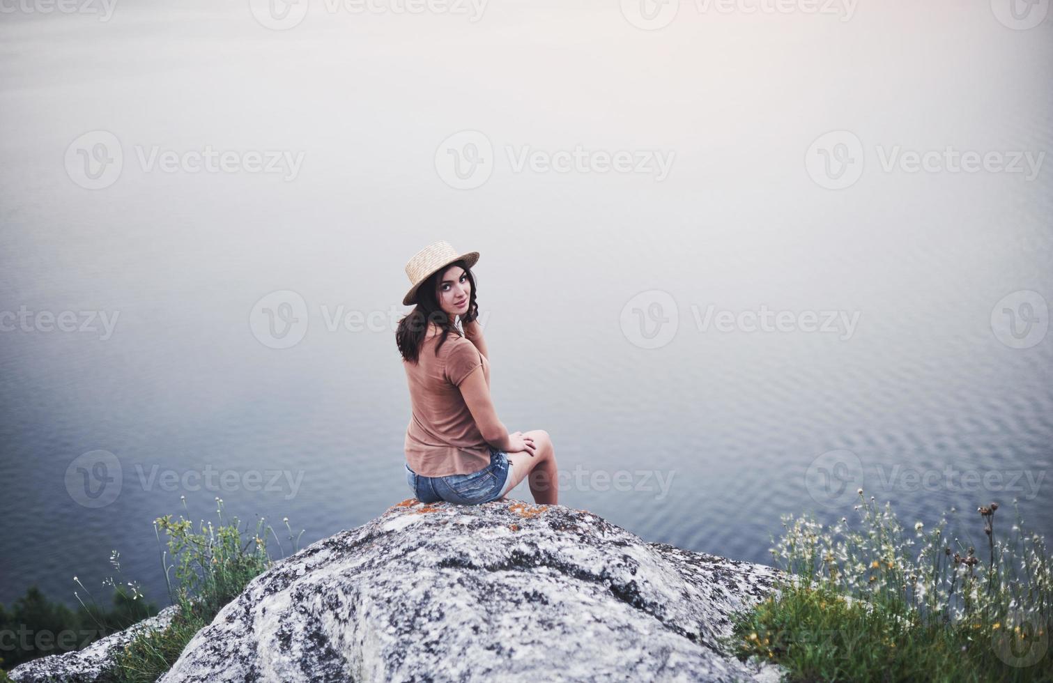 vista desde atrás. Atractiva chica turística posando en el borde de la montaña con un lago de agua clara en segundo plano. foto