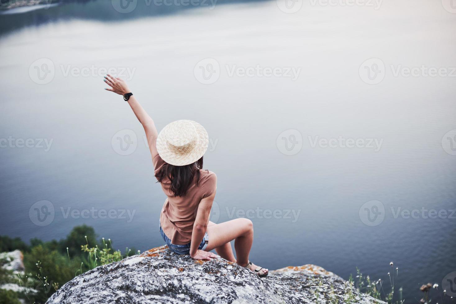 sintiendo libertad. Atractiva chica turística posando en el borde de la montaña con un lago de agua clara en segundo plano. foto