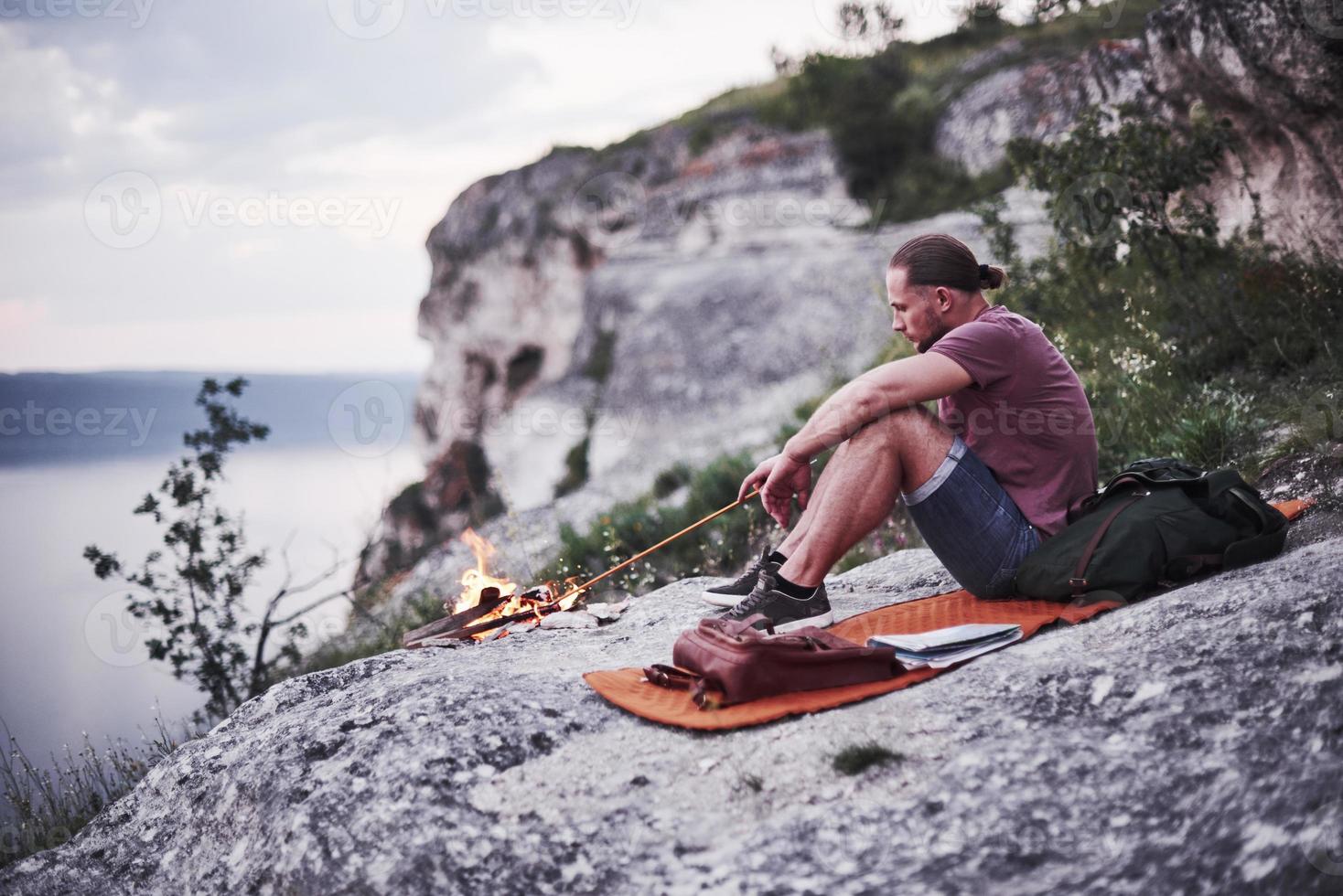 hombre solo sentado cerca de la fogata, tratando de mantener el fuego en el borde de la montaña foto