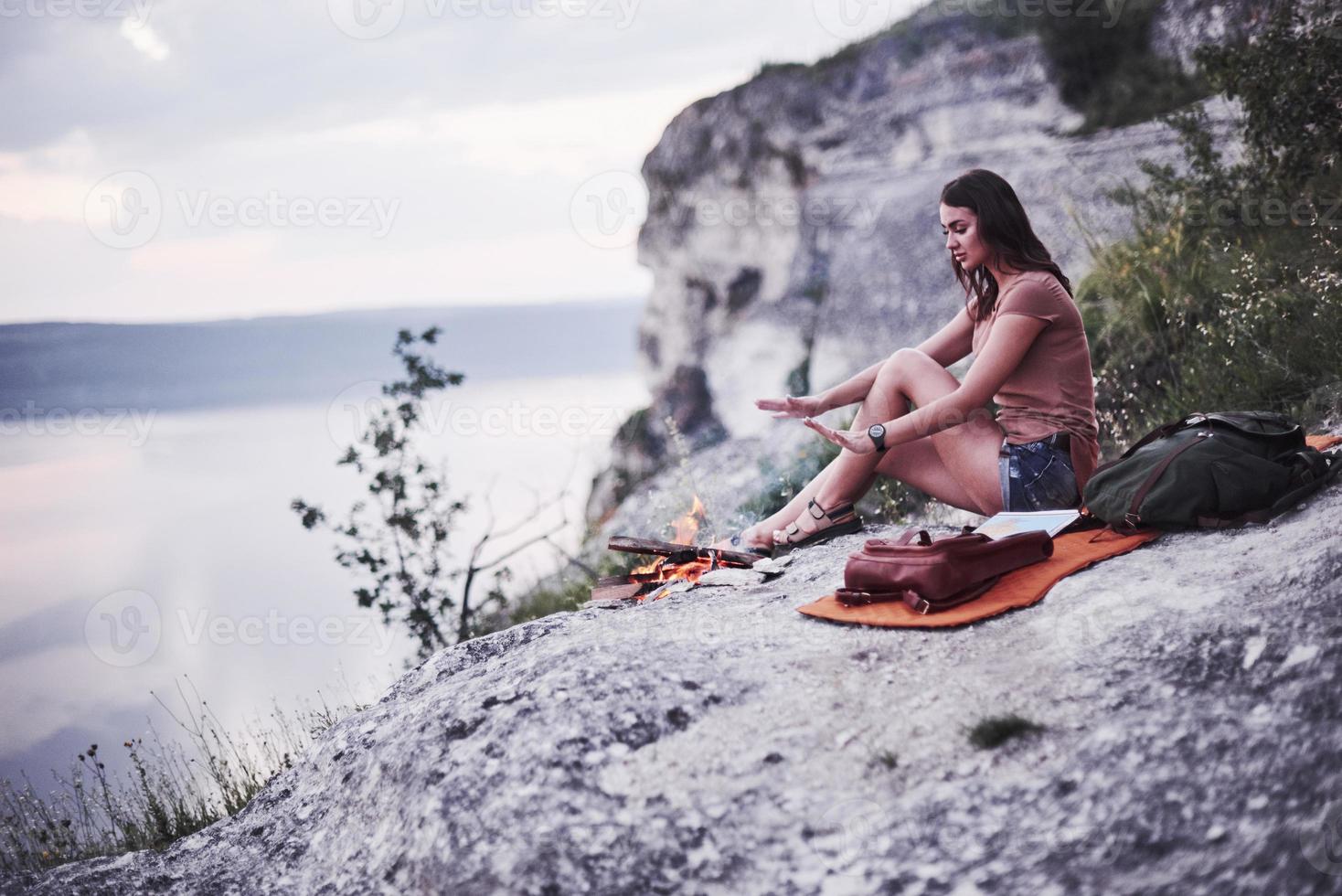 Girl tries to get warm from fire at quick made camp on the beautiful mountain photo