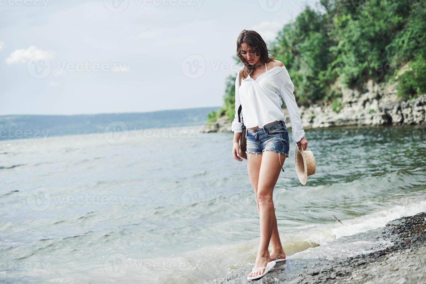 Hermosa chica modelo posando en la playa con fondo de acantilado con árboles foto