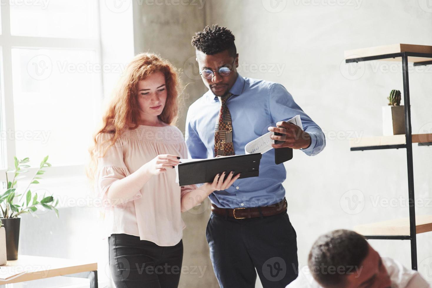 Black guy and redhead girl read the reports in the office with plants photo