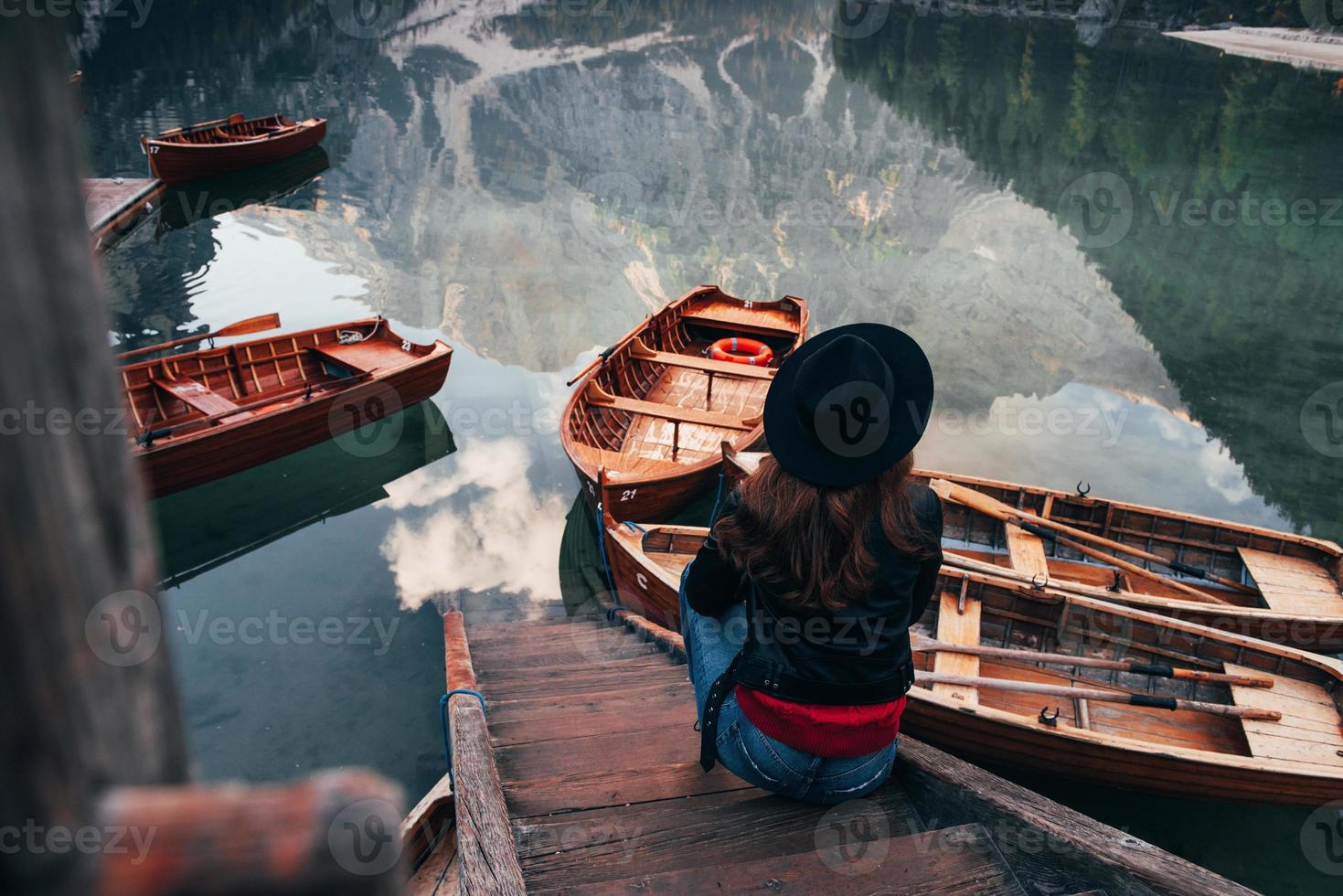 Muelle de madera. Mujer con sombrero negro disfrutando del majestuoso paisaje de montaña cerca del lago con barcos foto