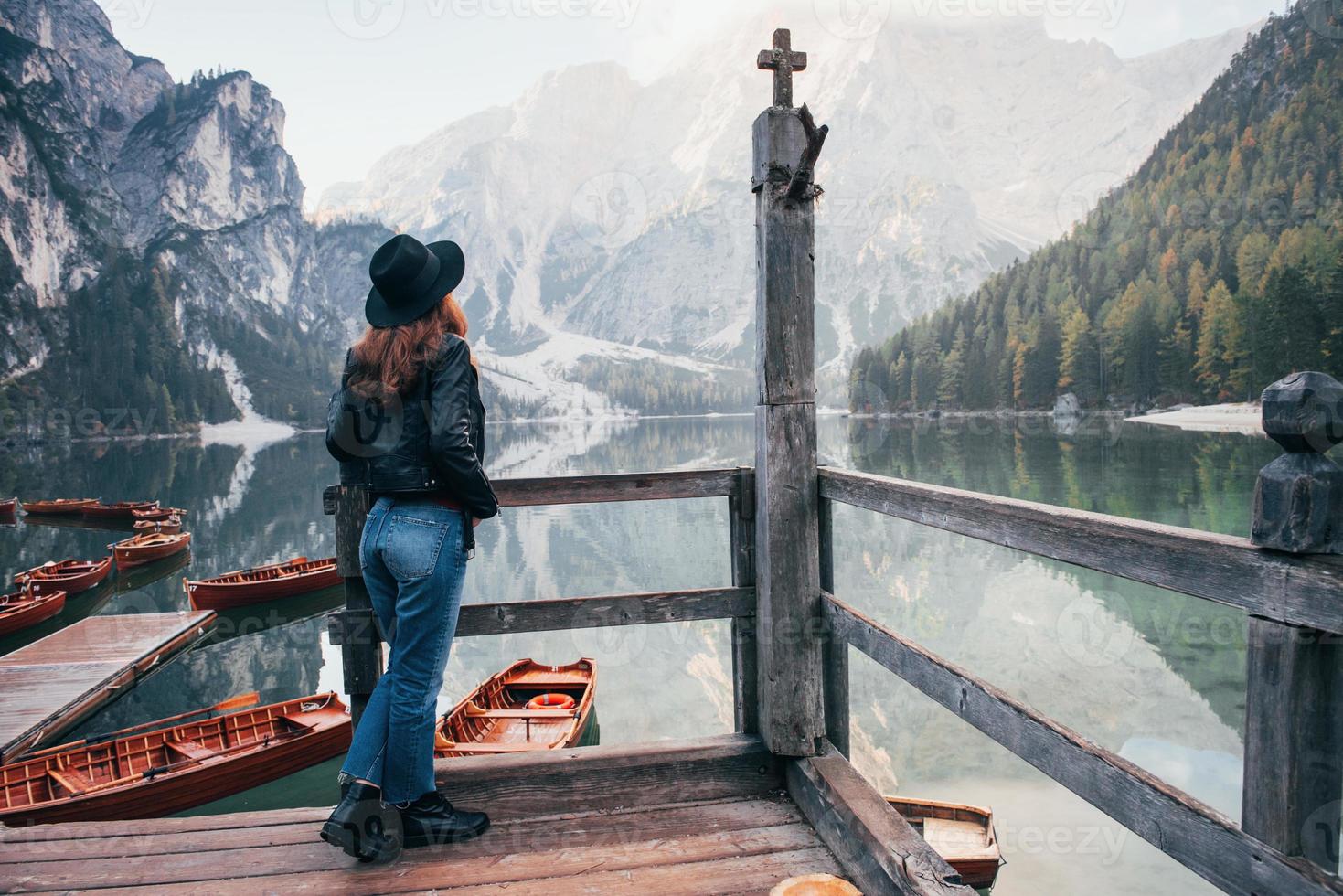 colinas y valles. Mujer con sombrero negro disfrutando del majestuoso paisaje de montaña cerca del lago con barcos foto