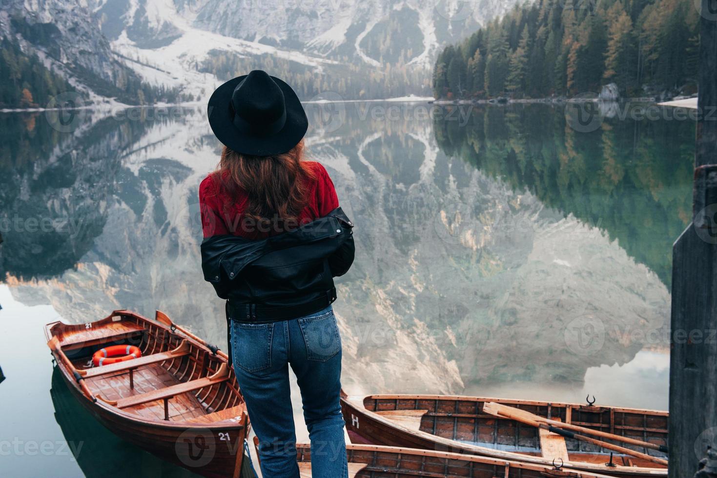 Look at this clean water. Woman in black hat enjoying majestic mountain landscape near the lake with boats photo