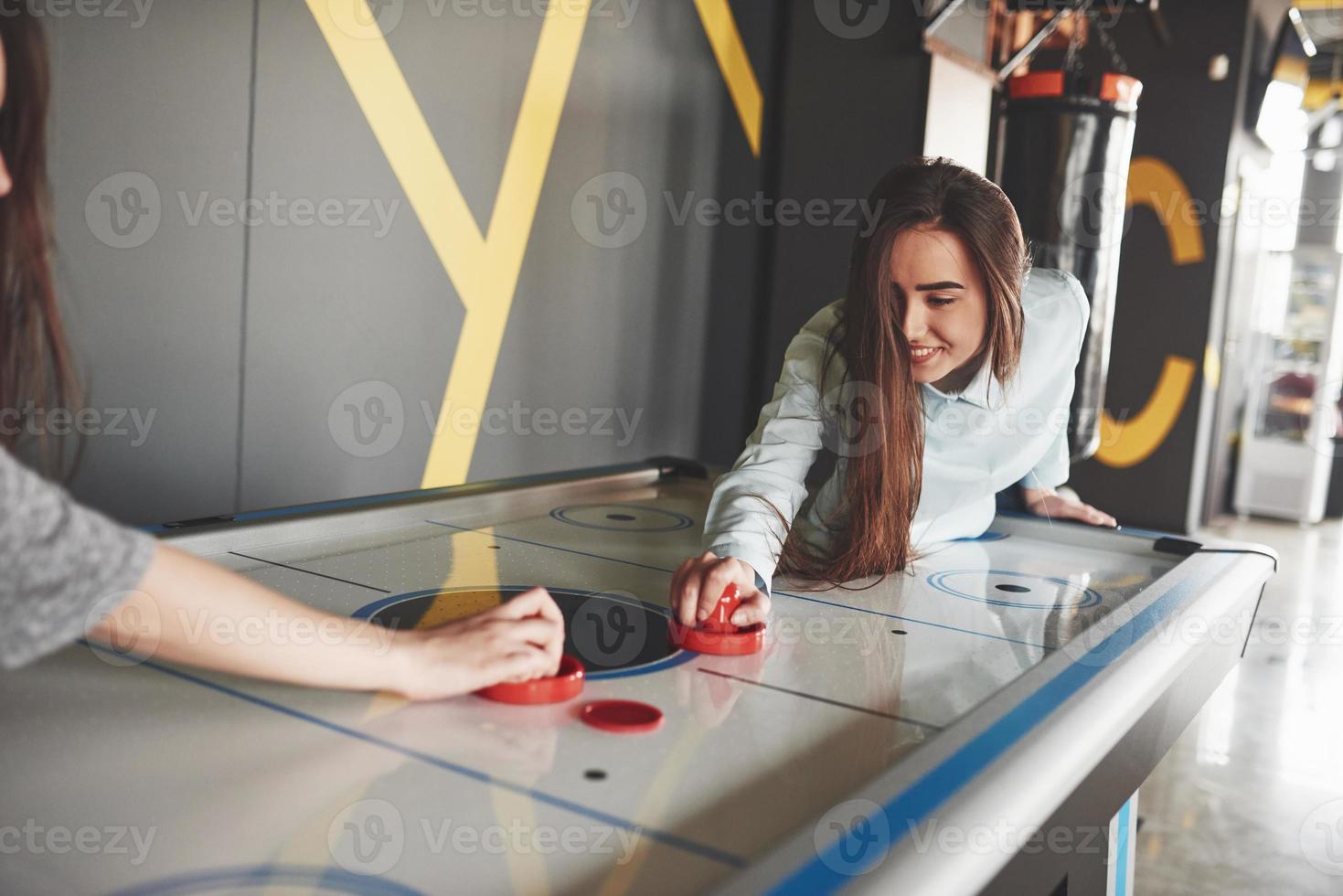 dos hermosas niñas gemelas juegan air hockey en la sala de juegos y se divierten foto