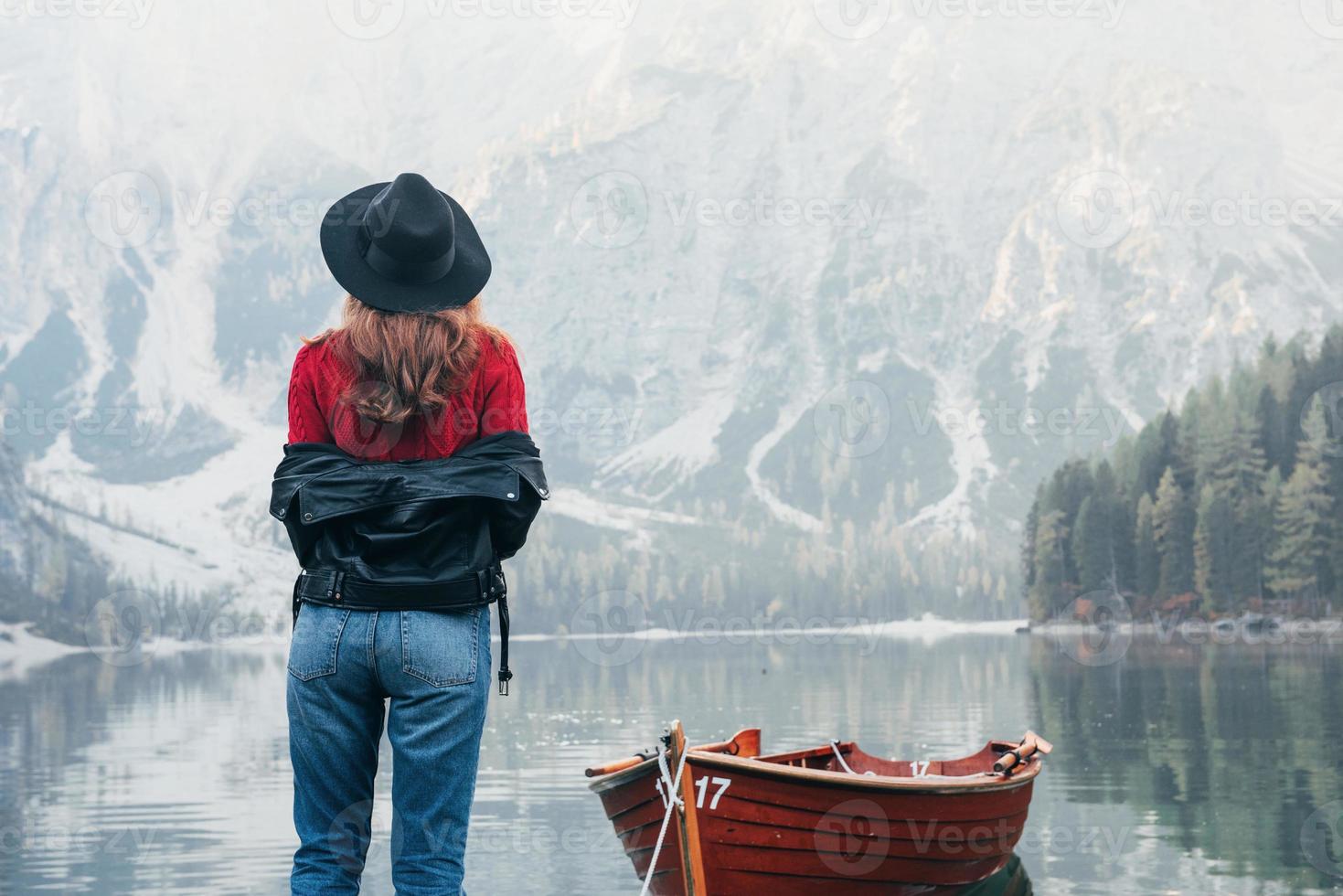 Such an awesome nature. Woman in black hat enjoying majestic mountain landscape near the lake with boat photo