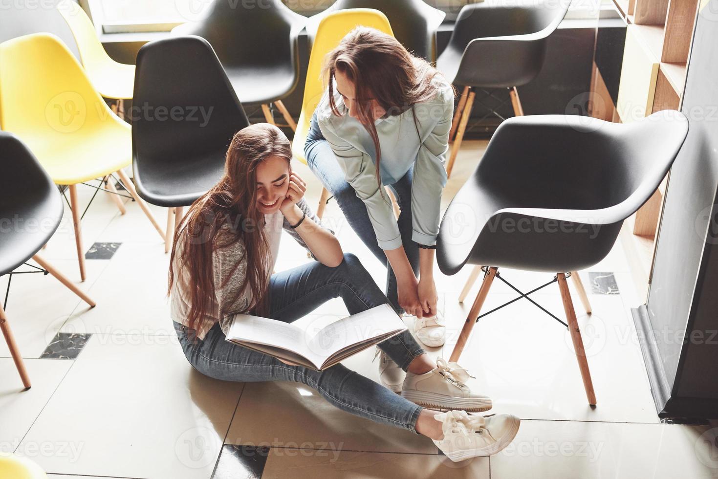 Two beautiful twin girls spend time read a book in library in the morning. Sisters relaxing in a cafe and having fun together photo