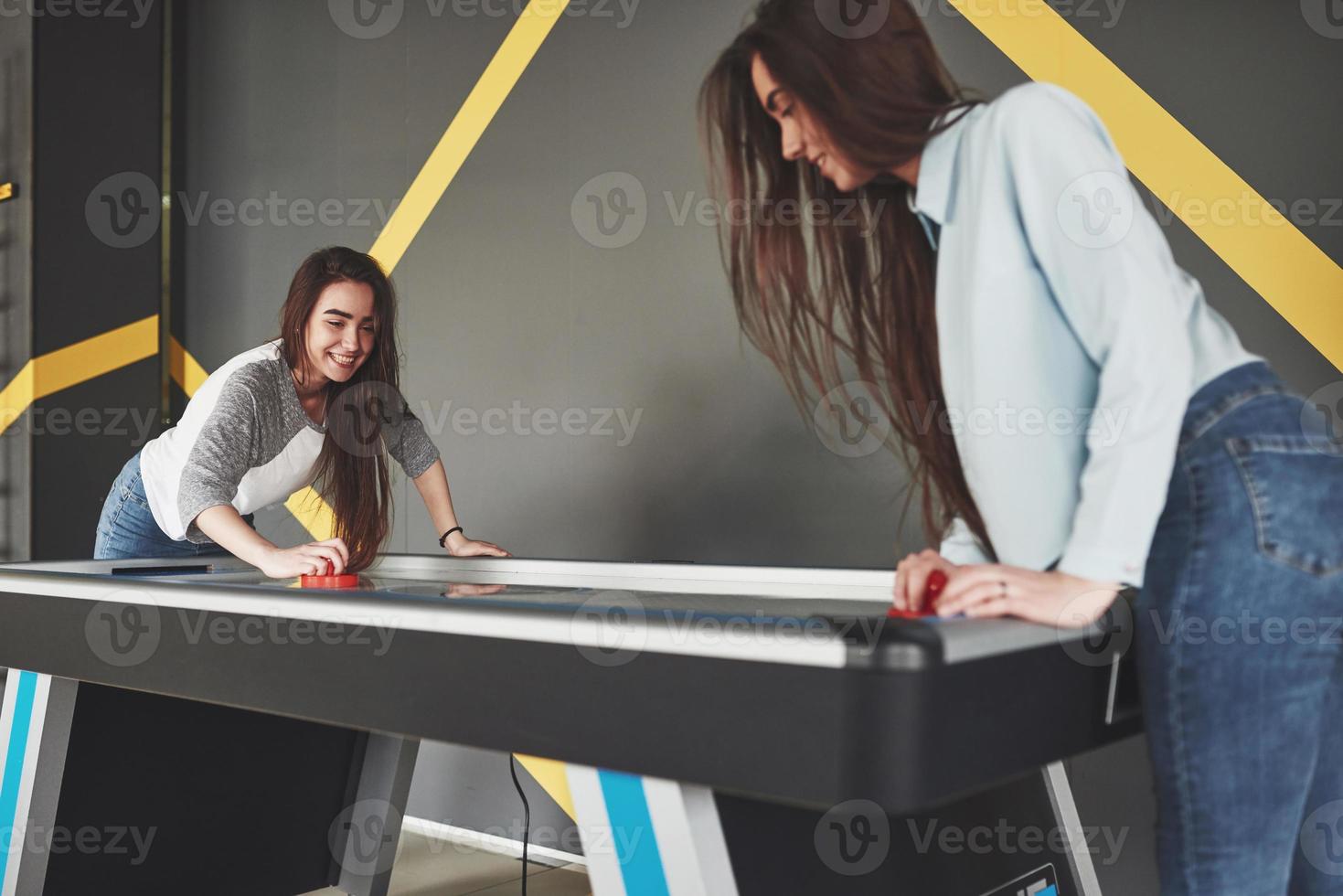 Two beautiful twin girls play air hockey in the game roomand have fun photo