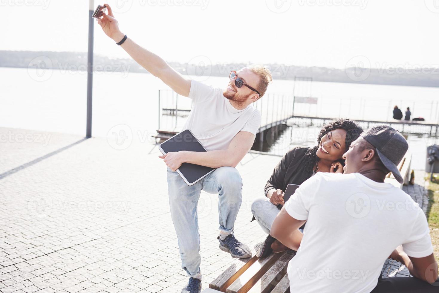 Beautiful multi ethnic friends using a laptop in the Street and make selphie. Youth lifestyle concept photo