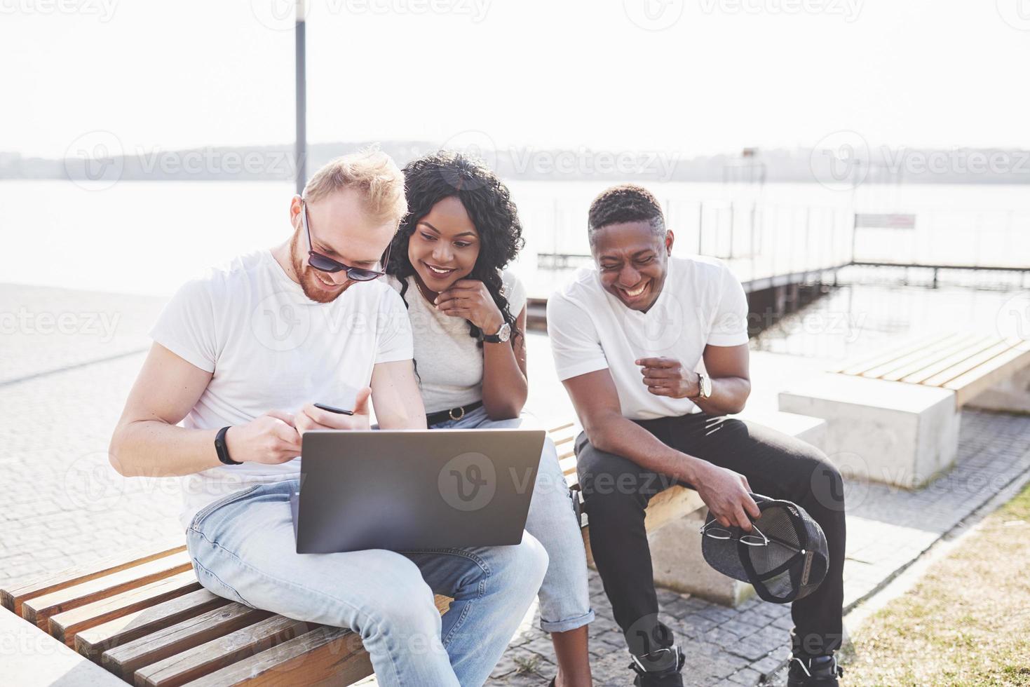 hermosos amigos multiétnicos usando una computadora portátil en la calle. concepto de estilo de vida juvenil foto