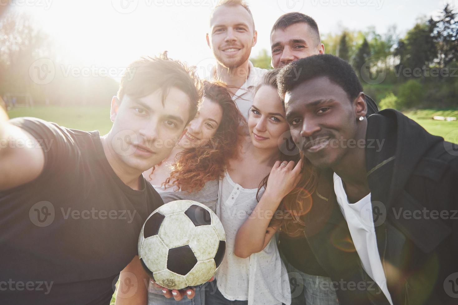 un grupo de amigos en ropa casual hacen sephi en el campo de fútbol. la gente se divierte y se divierte. descanso activo y puesta de sol escénica foto