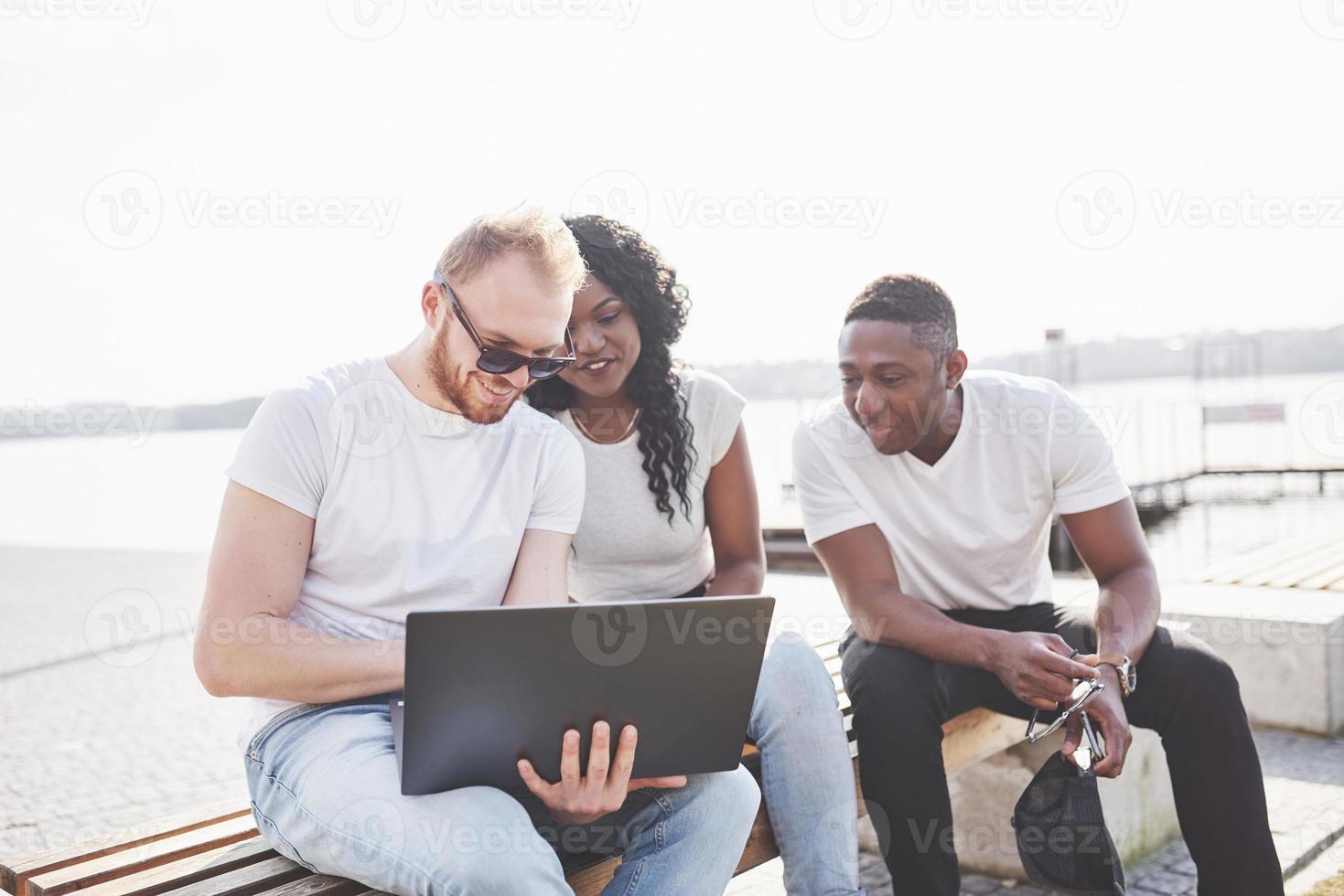 hermosos amigos multiétnicos usando una computadora portátil en la calle. concepto de estilo de vida juvenil foto