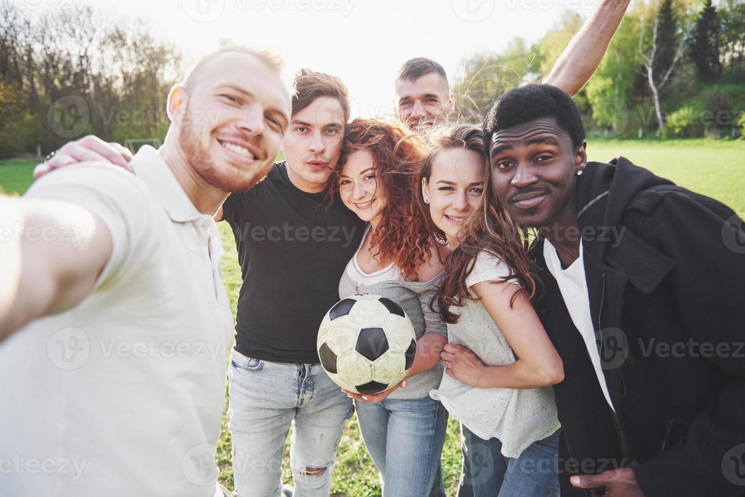 un grupo de amigos en ropa casual hacen sephi en el campo de fútbol. la gente se divierte y se divierte. descanso activo y puesta de sol escénica foto