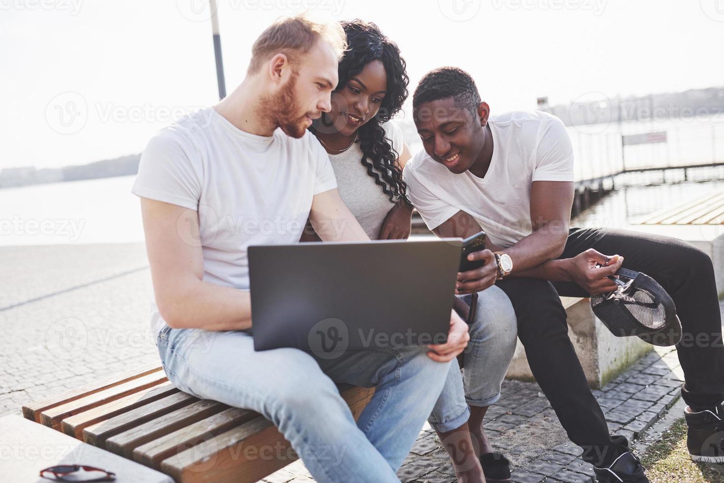 hermosos amigos multiétnicos usando una computadora portátil en la calle. concepto de estilo de vida juvenil foto