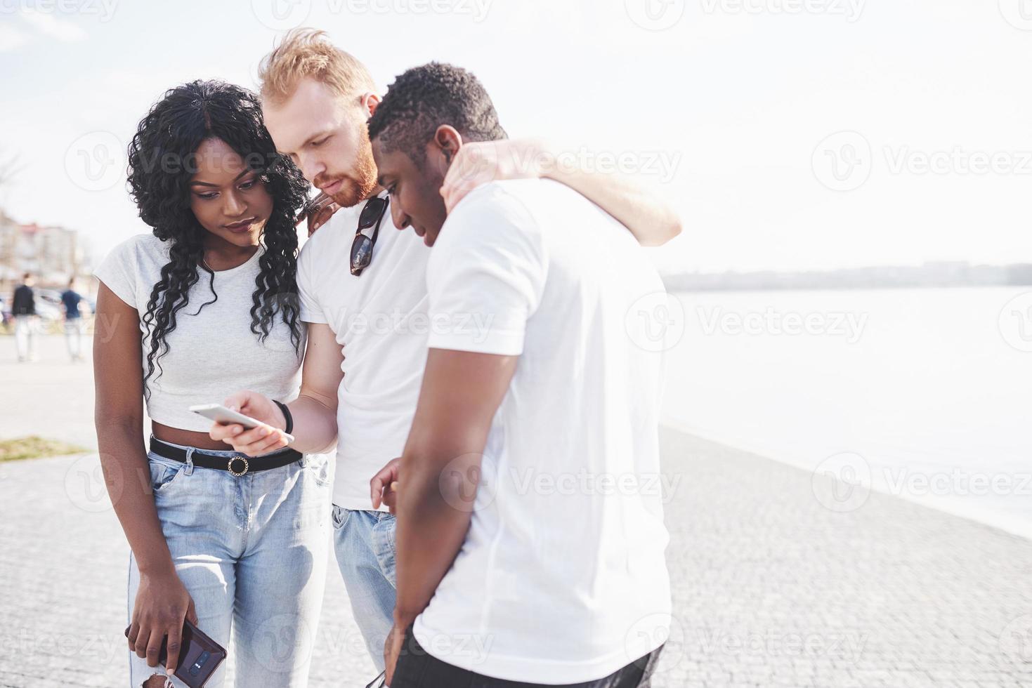 grupo de amigos felices multirraciales usando gadget al aire libre. concepto de felicidad y amistad multiétnica todos juntos contra el racismo foto