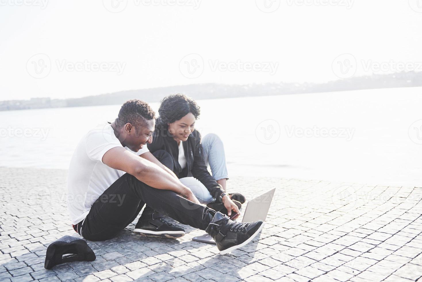 Dos amigos felices de estudiantes o socios comerciales están sentados al aire libre y disfrutan de una computadora portátil foto