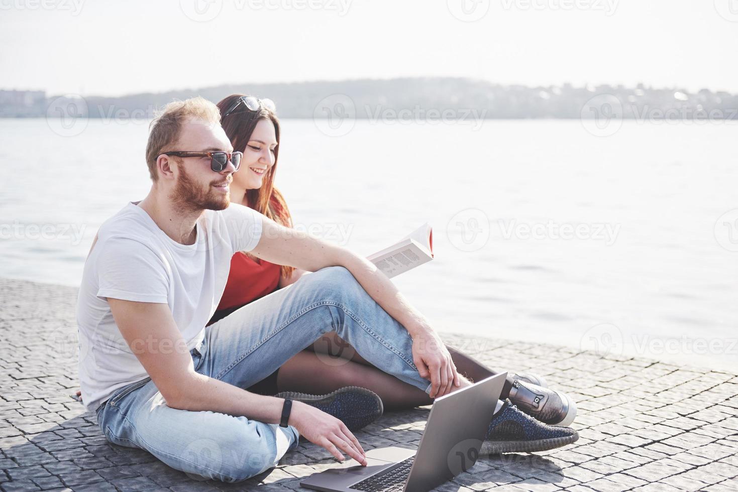 Dos estudiantes, chico y chica, están sentados al aire libre y disfrutando de una computadora portátil, estudiando al aire libre en un día soleado foto