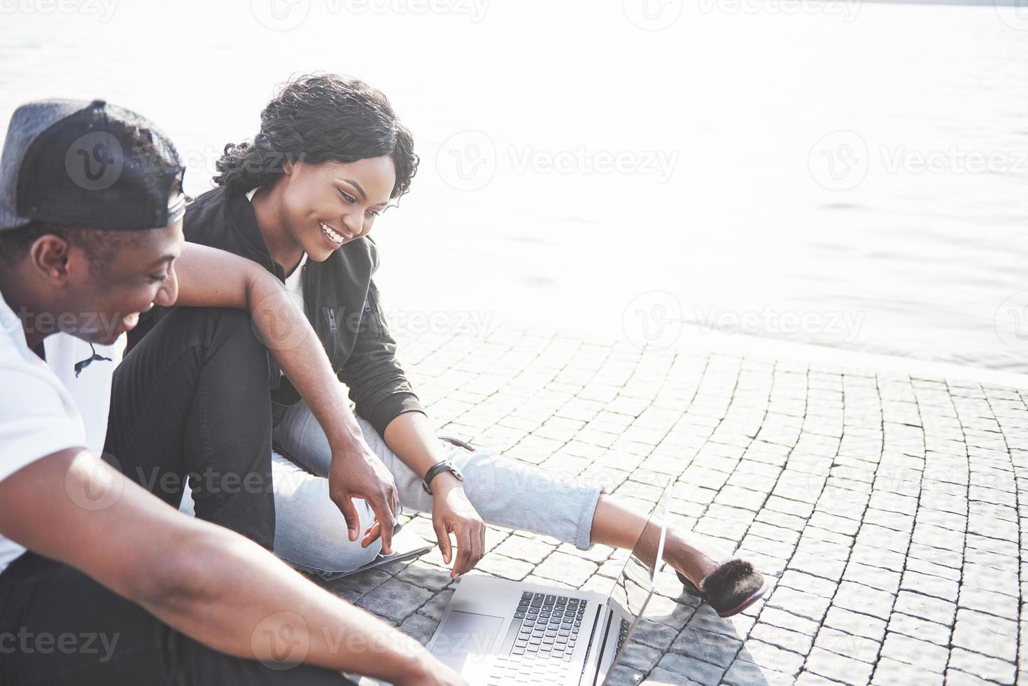 Dos amigos felices de estudiantes o socios comerciales están sentados al aire libre y disfrutan de una computadora portátil foto