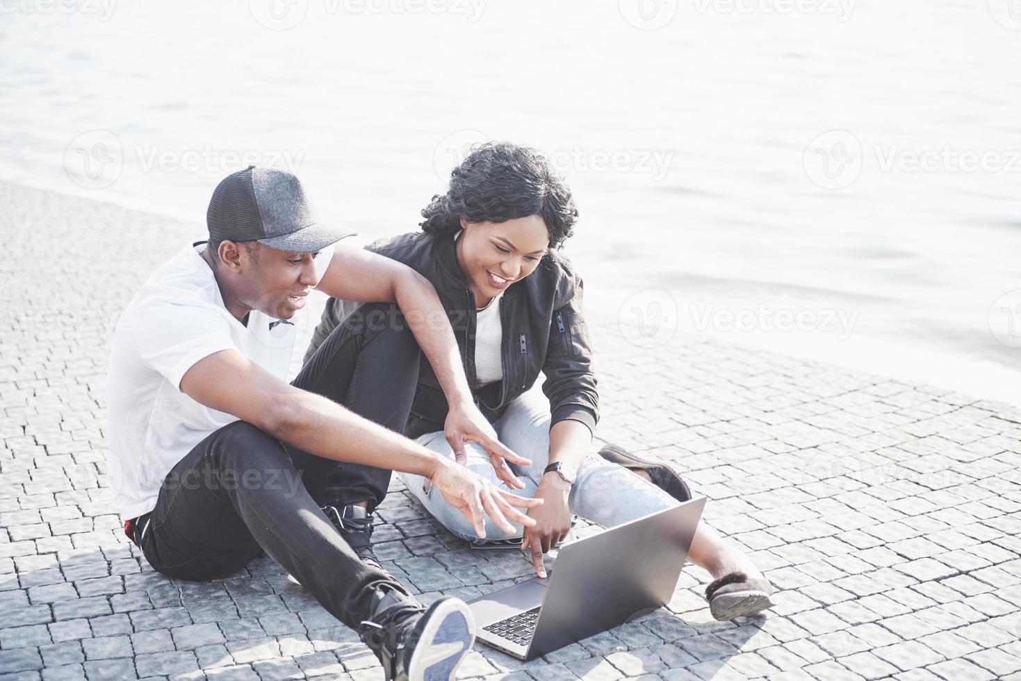 Dos amigos felices de estudiantes o socios comerciales están sentados al aire libre y disfrutan de una computadora portátil foto