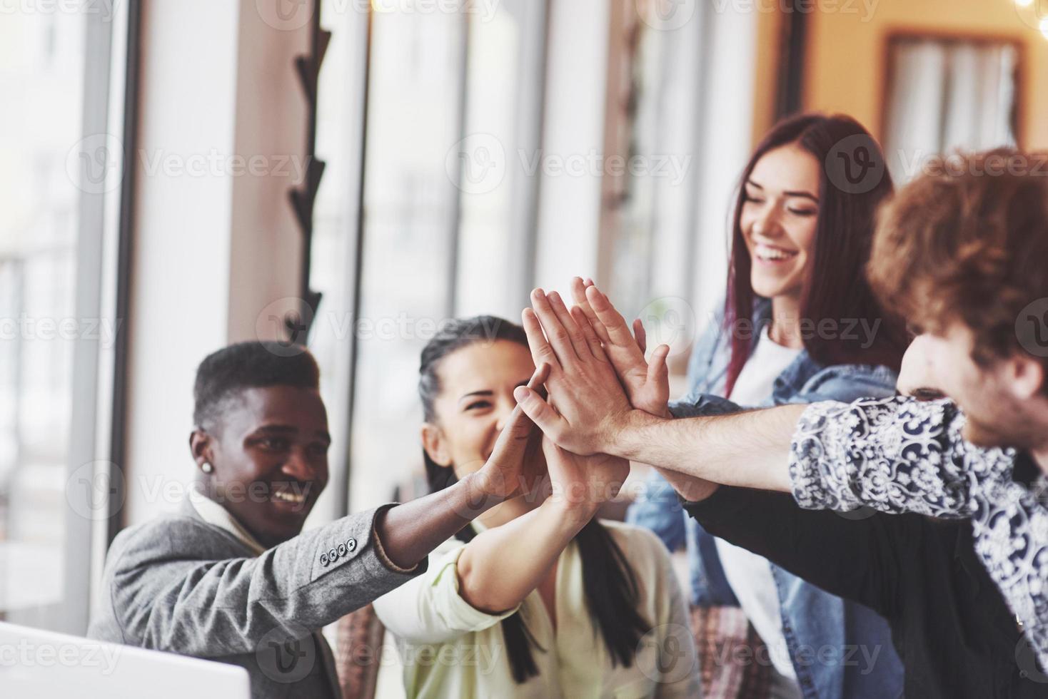 Happy young entrepreneurs in casual clothes at cafe table or in business office giving high fives to each other as if celebrating success or starting new project photo