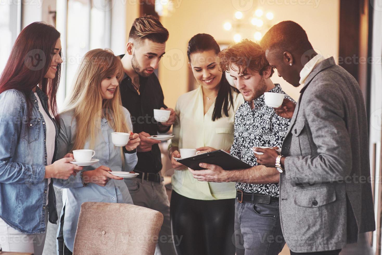 Los empresarios exitosos están usando aparatos, hablando y sonriendo durante la pausa para el café en la oficina. foto