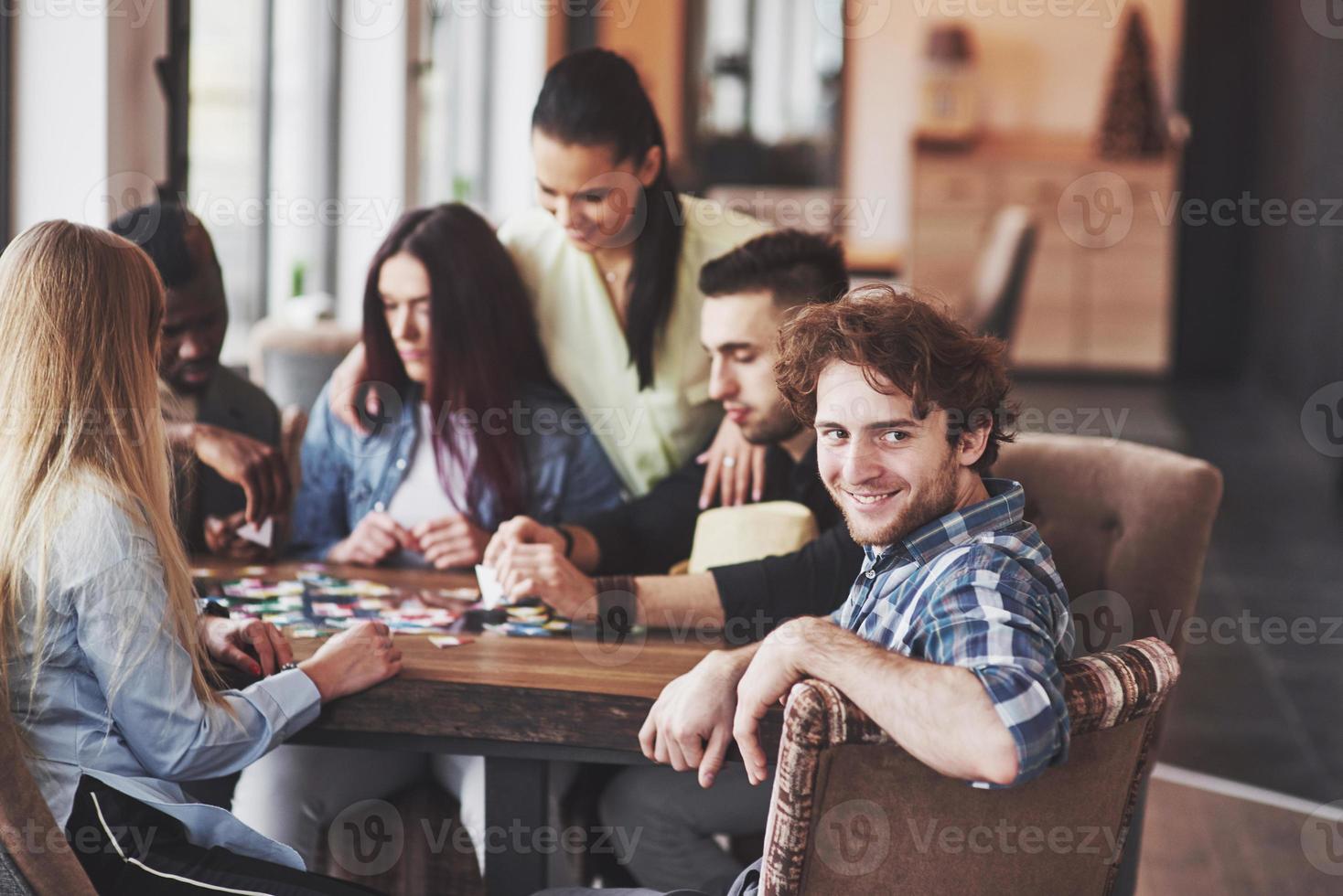Group of creative multietnic friends sitting at wooden table. People having fun while playing board game photo
