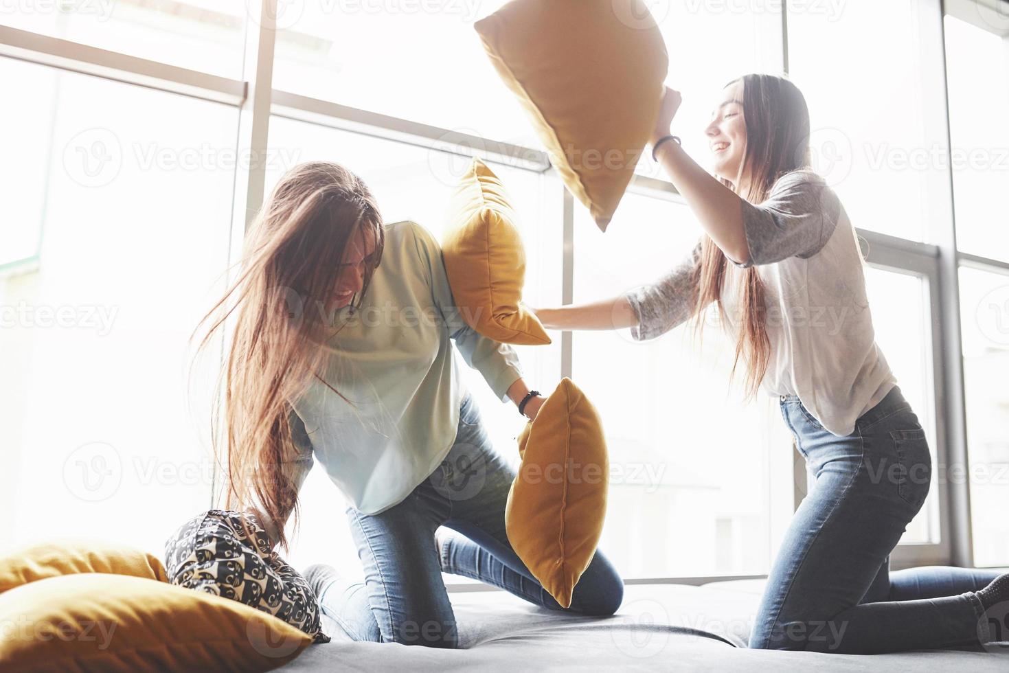 Two beautiful young twins sisters spending time together and are battling with pillows. Siblings having fun at home concept photo