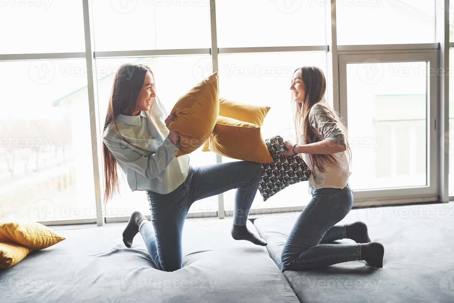 Two beautiful young twins sisters spending time together and are battling with pillows. Siblings having fun at home concept photo