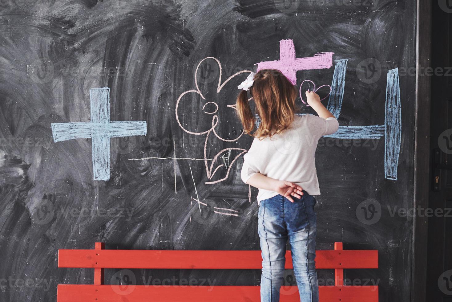 dibujo de niña rizada con crayón de color en la pared. obras de niño. lindo alumno escribiendo en la pizarra foto